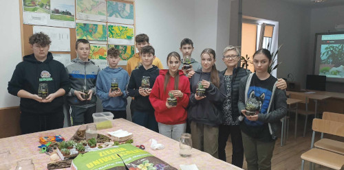 uczniowie klasy ósmej stoją i trzymają swoje prace florystyczne, wśród nich stoi również nauczycielka ZCKR, która prowadziła warsztaty.