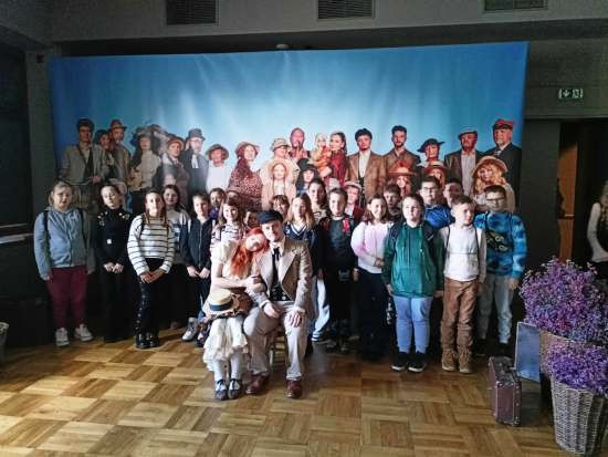 Uczniowie klas 4 i&nbsp;6 stoją z&nbsp;aktorami w&nbsp;kostiumach na tle dekoracji teatralnej po spektaklu „Ania z&nbsp;Zielonego Wzgórza” w&nbsp;Gorlickim Centrum Kultury.